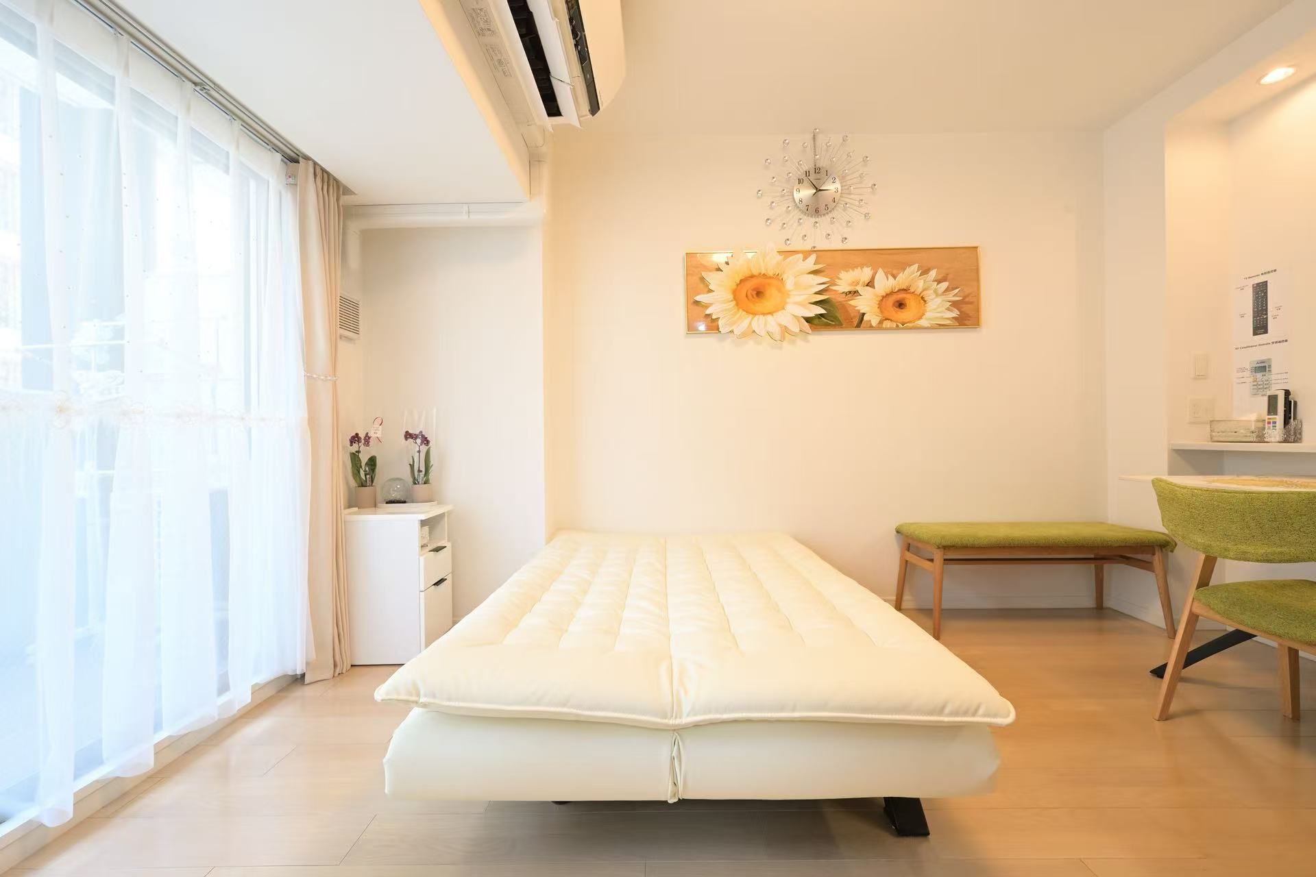 A room with a bed, a small table, a chair, and a wall clock.