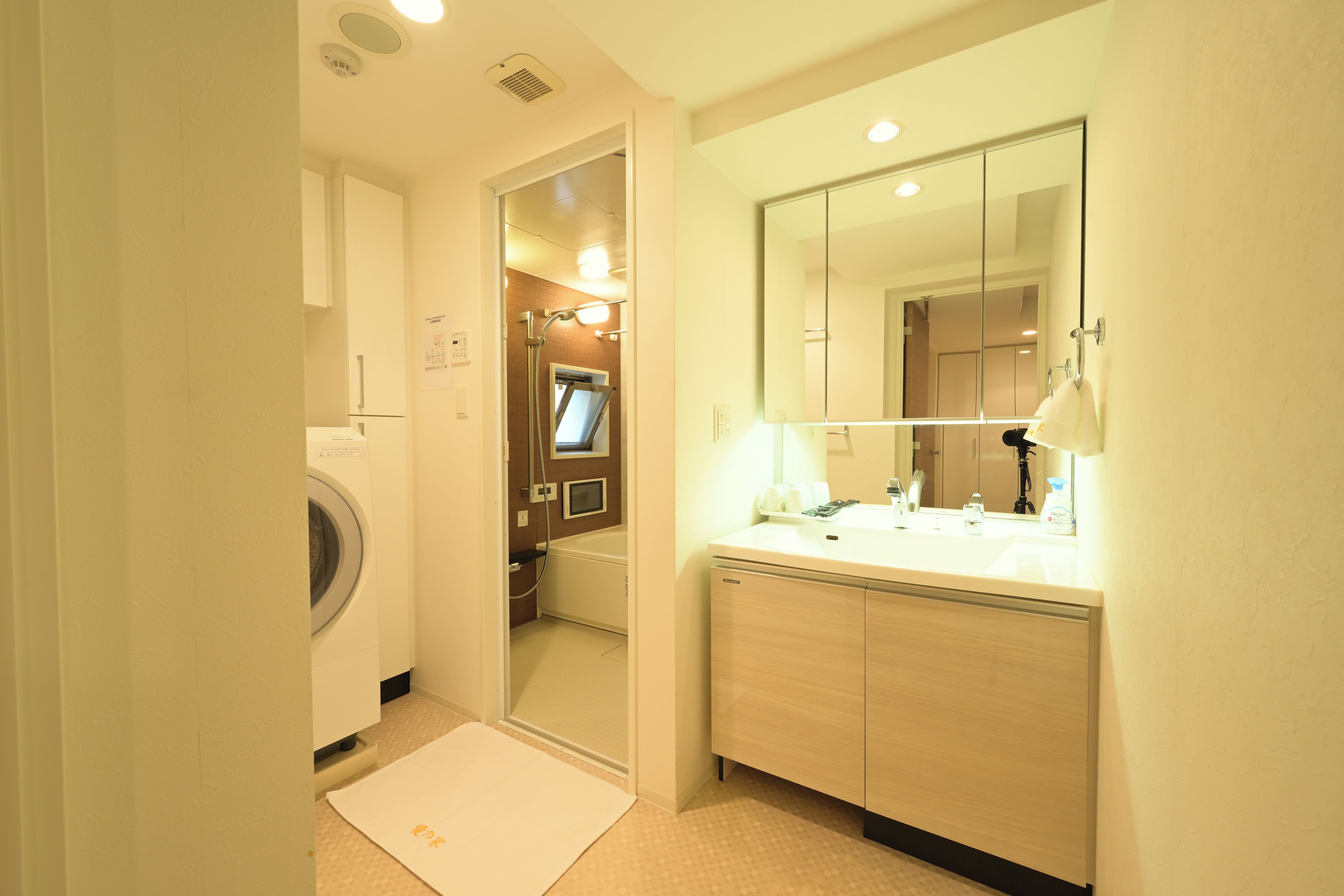 A hotel bathroom with a washing machine, a bathtub, a sink with a mirror, and a towel rack.