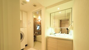 Casa de banho de hotel com máquina de lavar roupa, banheira, pia com espelho e porta-toalhas.