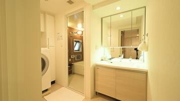 A hotel bathroom with a washing machine, a bathtub, a sink with a mirror, and a towel rack.