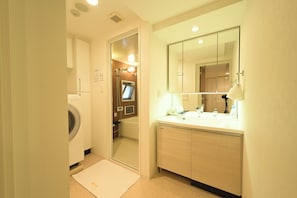 Een hotelbadkamer met een wasmachine, een bad, een wastafel met spiegel en een handdoekrek.