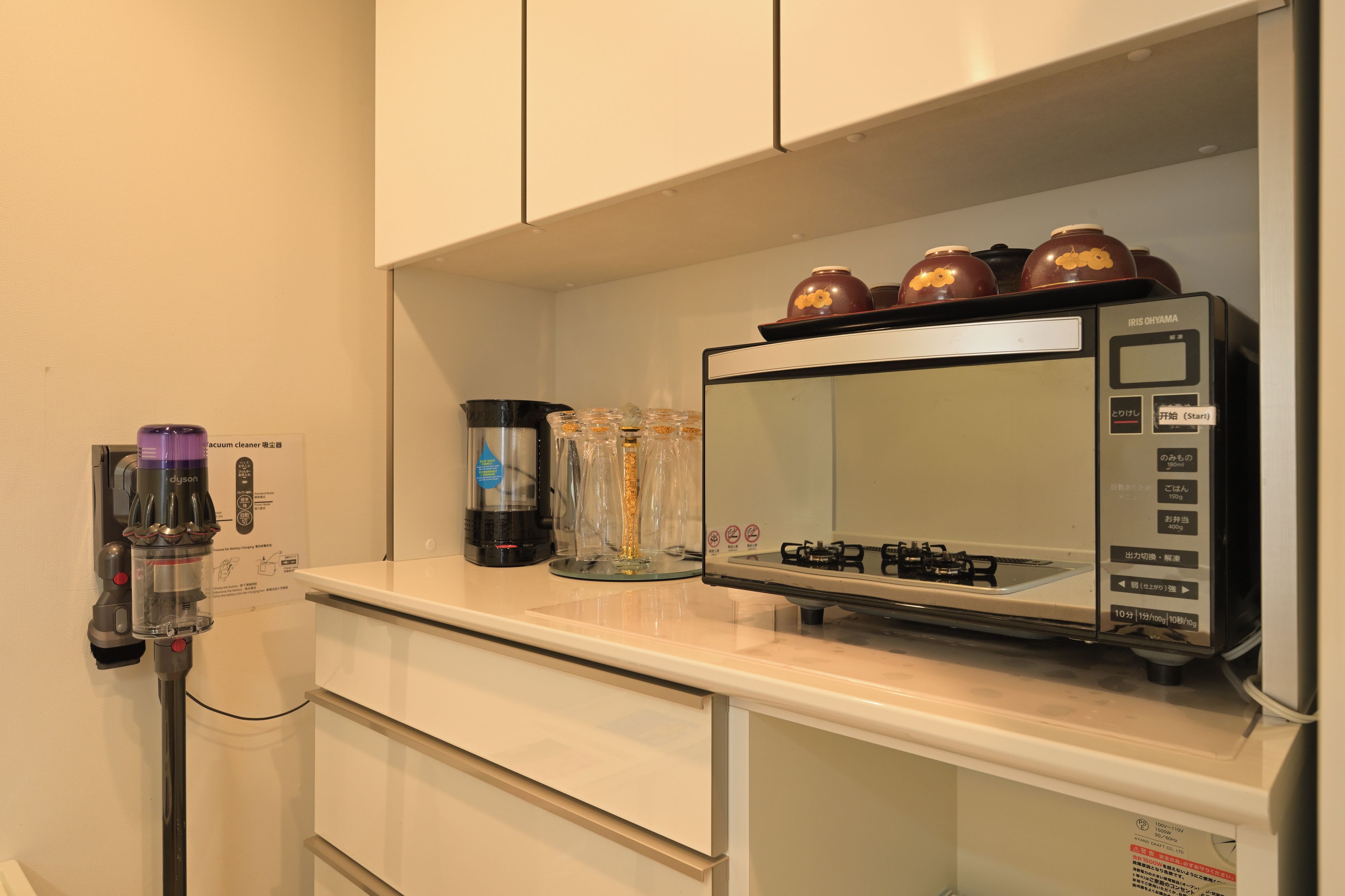 A kitchen with a microwave, a Dyson vacuum cleaner, and a coffee maker on the counter.