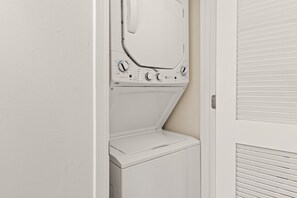 A compact, white laundry room with a front-loading washing machine and a dryer. - Destin West Pelican 308 - Amazing Views of the 700ft Lazy River & Emerald Waters! (Fort Walton Beach)