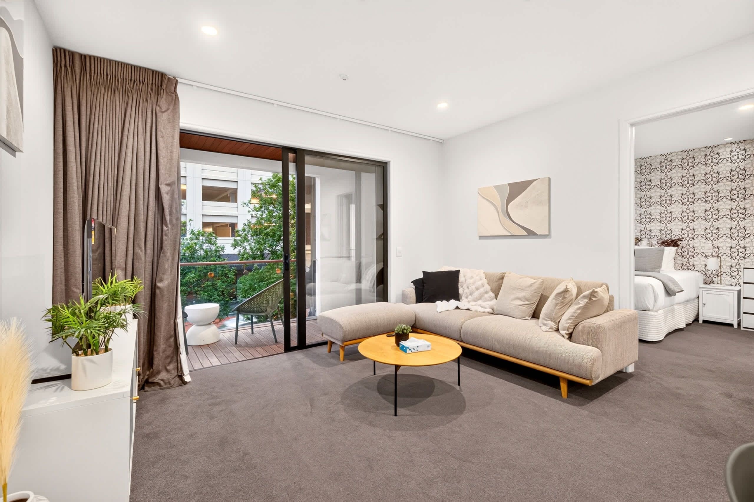 A modern living room with a sofa, a coffee table, and a balcony with a view of greenery.