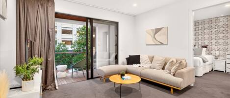 A modern living room with a sofa, a coffee table, and a balcony with a view of greenery.