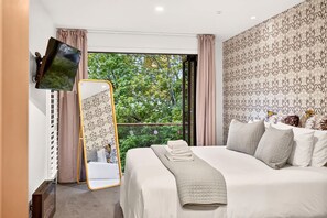 Una camera d'albergo con un letto grande, una televisione a schermo piatto fissata al muro, una finestra con tende e carta da parati decorata.