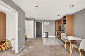 Une cuisine moderne dotée d’appareils électroménagers intégrés, un coin repas avec une table et des chaises blanches, et un couloir avec une porte donnant sur une autre pièce.