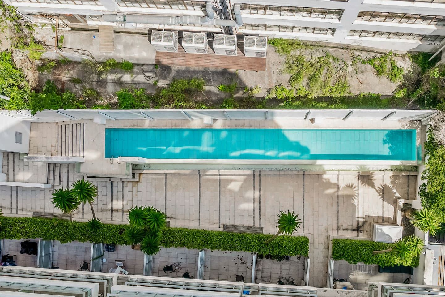 An aerial view of a building with a swimming pool, surrounded by greenery and a paved area.
