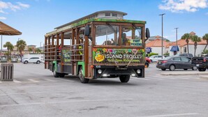 A wooden island trolley with "Ride Free" and "Ride Green" signage, parked on a street with cars and buildings in the background. - Sabine Yacht & Racquet Club 6C | Spectacular Pensacola Beachfront Views | Beach Svc (Pensacola Beach)