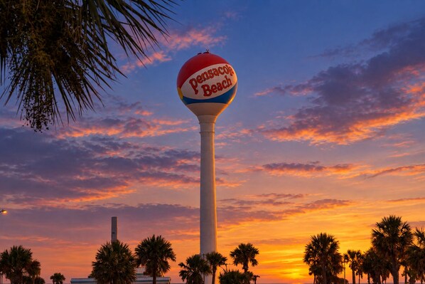 Une haute colonne blanche surmontée d’une sphère portant l’inscription « Pensacola Beach ».