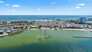 Vue aérienne d’une zone de villégiature côtière comprenant un port de plaisance, une plage et divers bâtiments, notamment des hôtels et des restaurants.