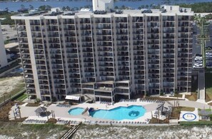 A high-rise hotel with multiple balconies, a swimming pool, and a parking area. - Phoenix East 110 | Beachside Outdoor Pool | Gulf Views | Pickleball Court (Orange Beach)
