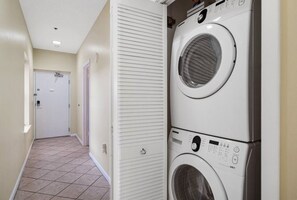 A laundry room with two stacked front-loading washing machines and a door at the end of the hallway. - Phoenix East 110 | Beachside Outdoor Pool | Gulf Views | Pickleball Court (Orange Beach)
