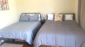 Una habitación con dos camas, cada una con cabecera y almohadas, una mesita de noche con lámpara y una obra de arte colgada en la pared.