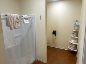 Ein Badezimmer mit Dusche, Handtuchhalter, Seifenspender und Ablage mit gefalteten Handtüchern.