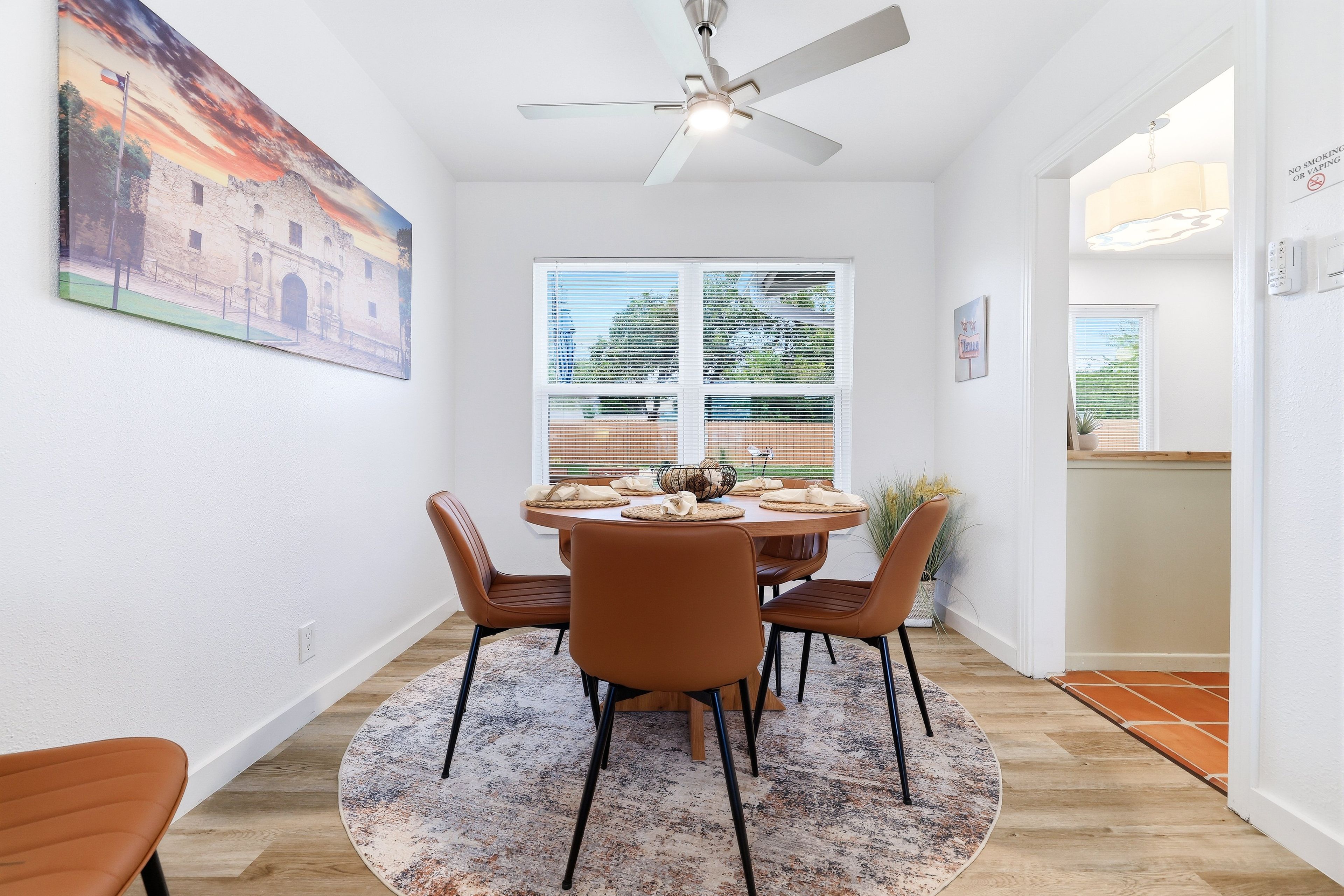 Un coin repas comprenant une table ronde, quatre chaises, un ventilateur de plafond et une fenêtre avec des stores.