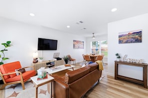 A modern living room with a leather sofa, a dining table, and a flat-screen TV mounted on the wall. - Agave - A Birdy Vacation Rental (San Antonio)