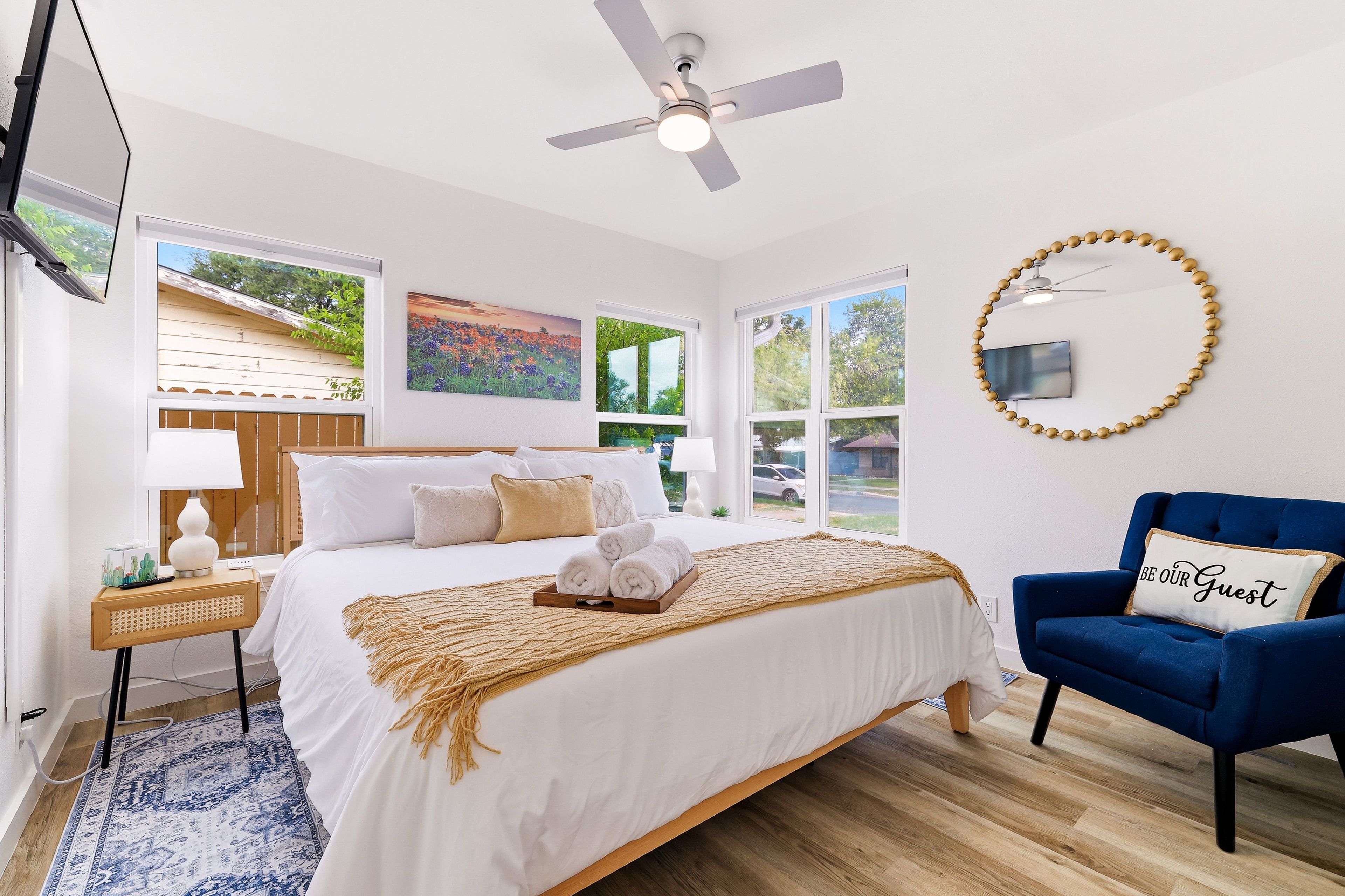 A bedroom with a bed, a blue armchair, a ceiling fan, and a window with a view of greenery.