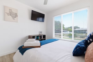 A bedroom with a large bed, a TV mounted on the wall, a bookshelf, and a window with blinds. - Agave - A Birdy Vacation Rental (San Antonio)