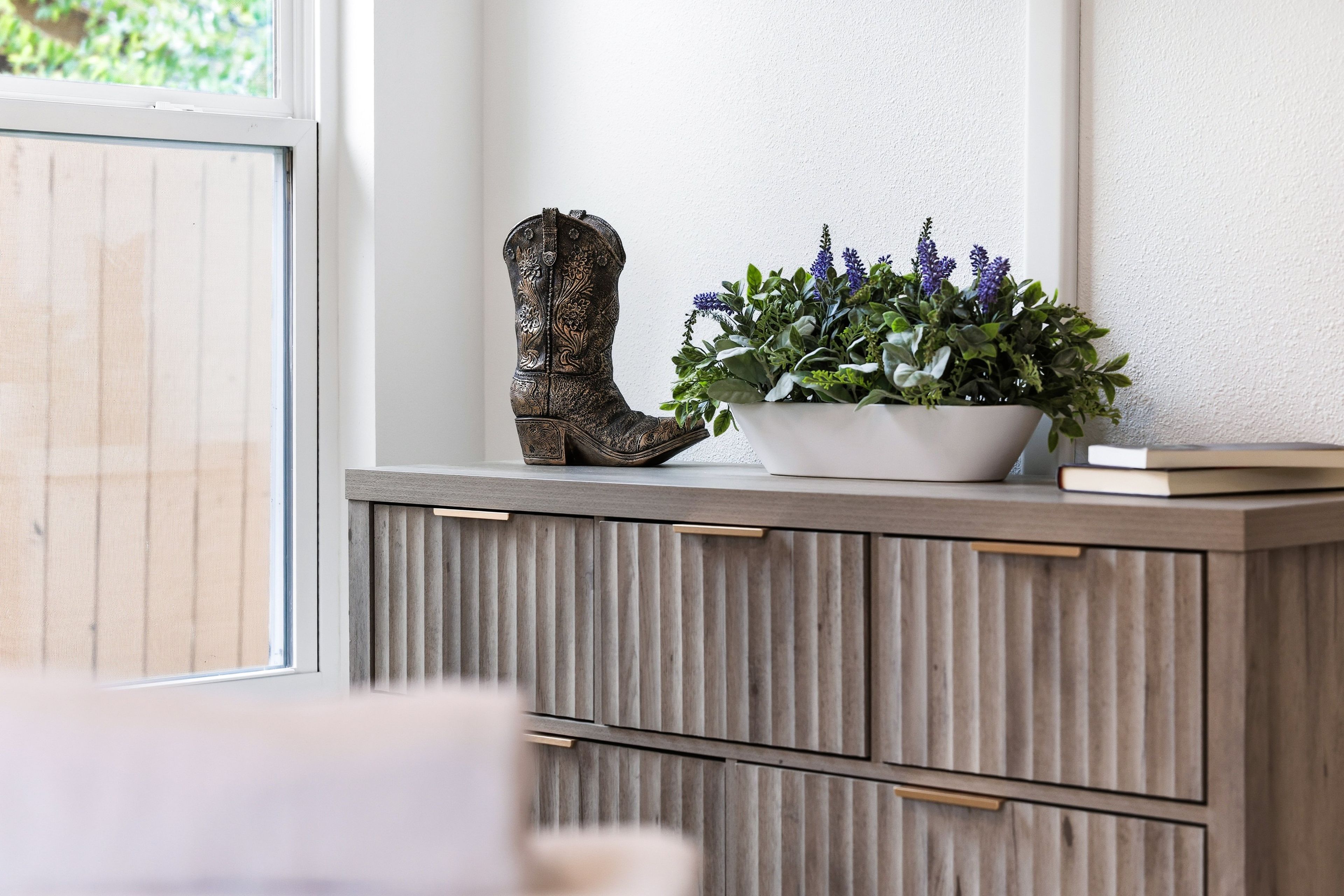 Ein Holzkabinett mit einer verzierten Stiefel und einem Blumentopf mit violetten Blüten.