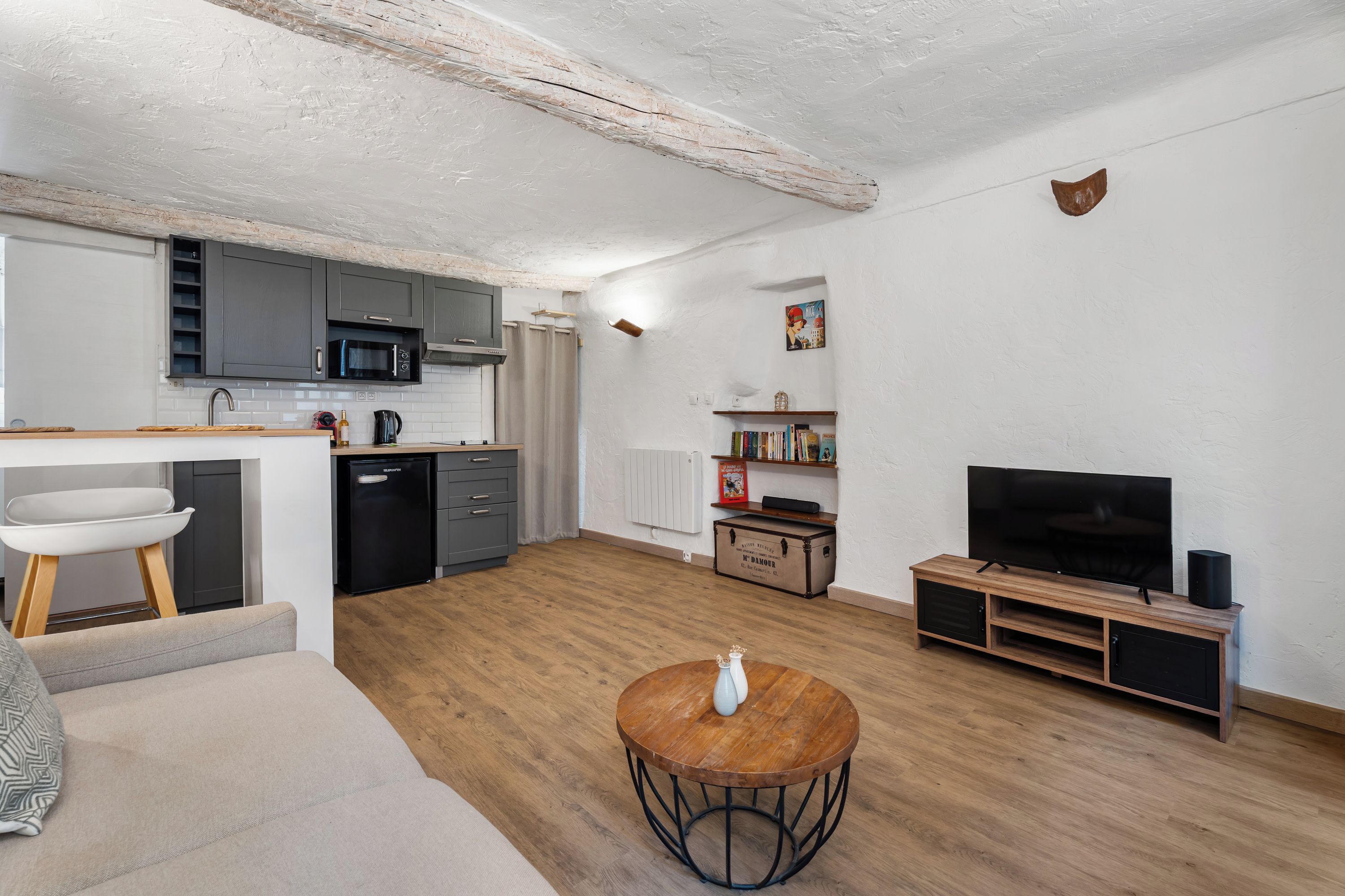 A modern living space with a kitchen, dining area, and a seating area with a round wooden table.