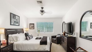 Une chambre d’hôtel comprenant un lit, une table de chevet, une lampe, une commode, une télévision et un grand miroir.