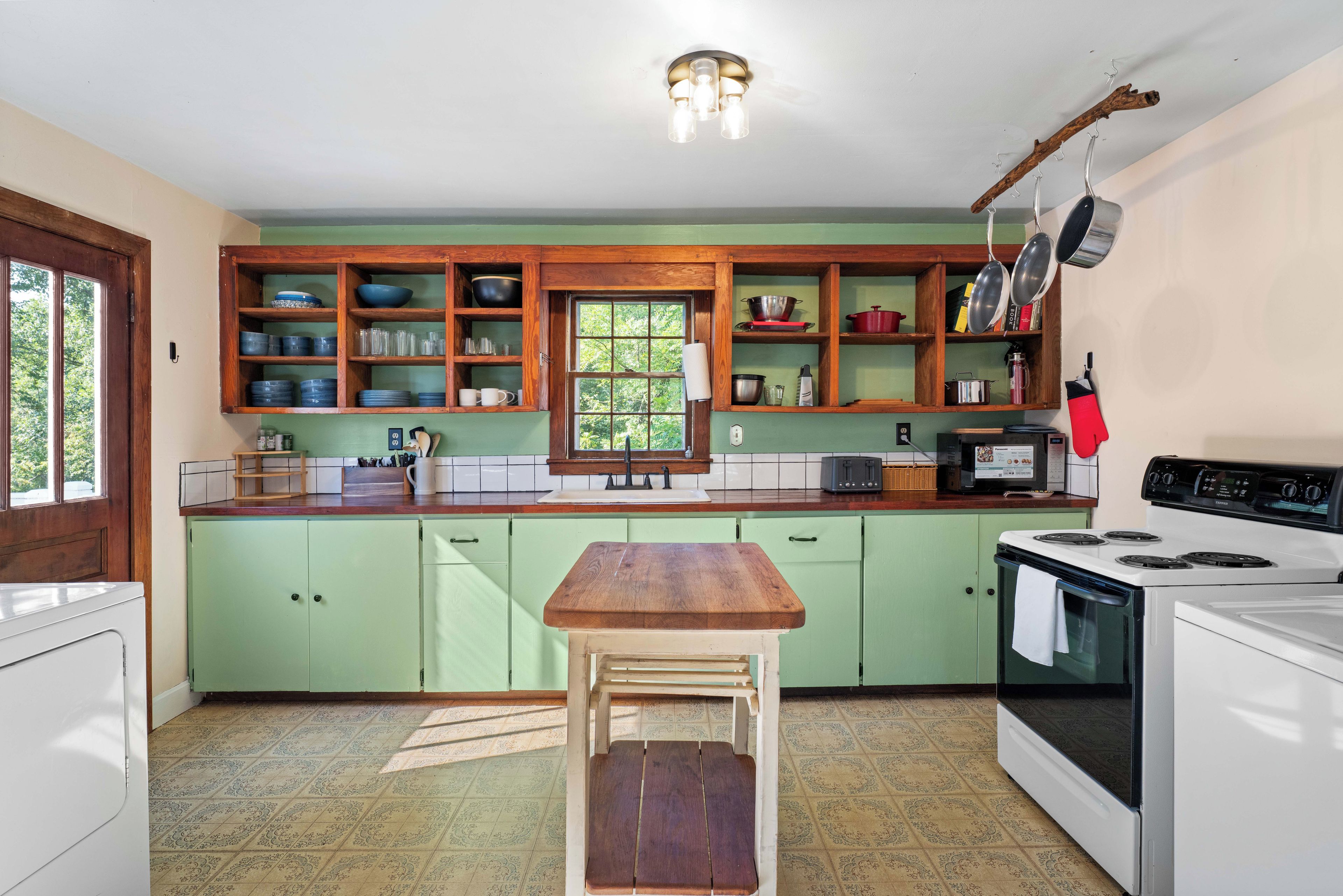 Een keuken met houten kasten, een houten tafel, een fornuis en een raam.