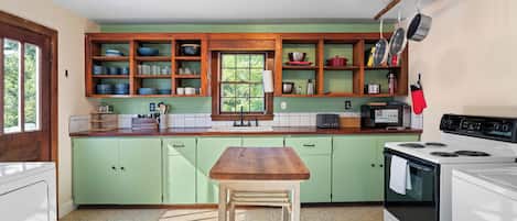 Una cocina con armarios de madera, una mesa de madera, una estufa y un ventanal.
