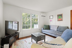 A living room with a television, a sofa, a coffee table, and a window with a view of trees. - Cozy Cottage Near Charlottesville & Wine Country (Charlottesville)