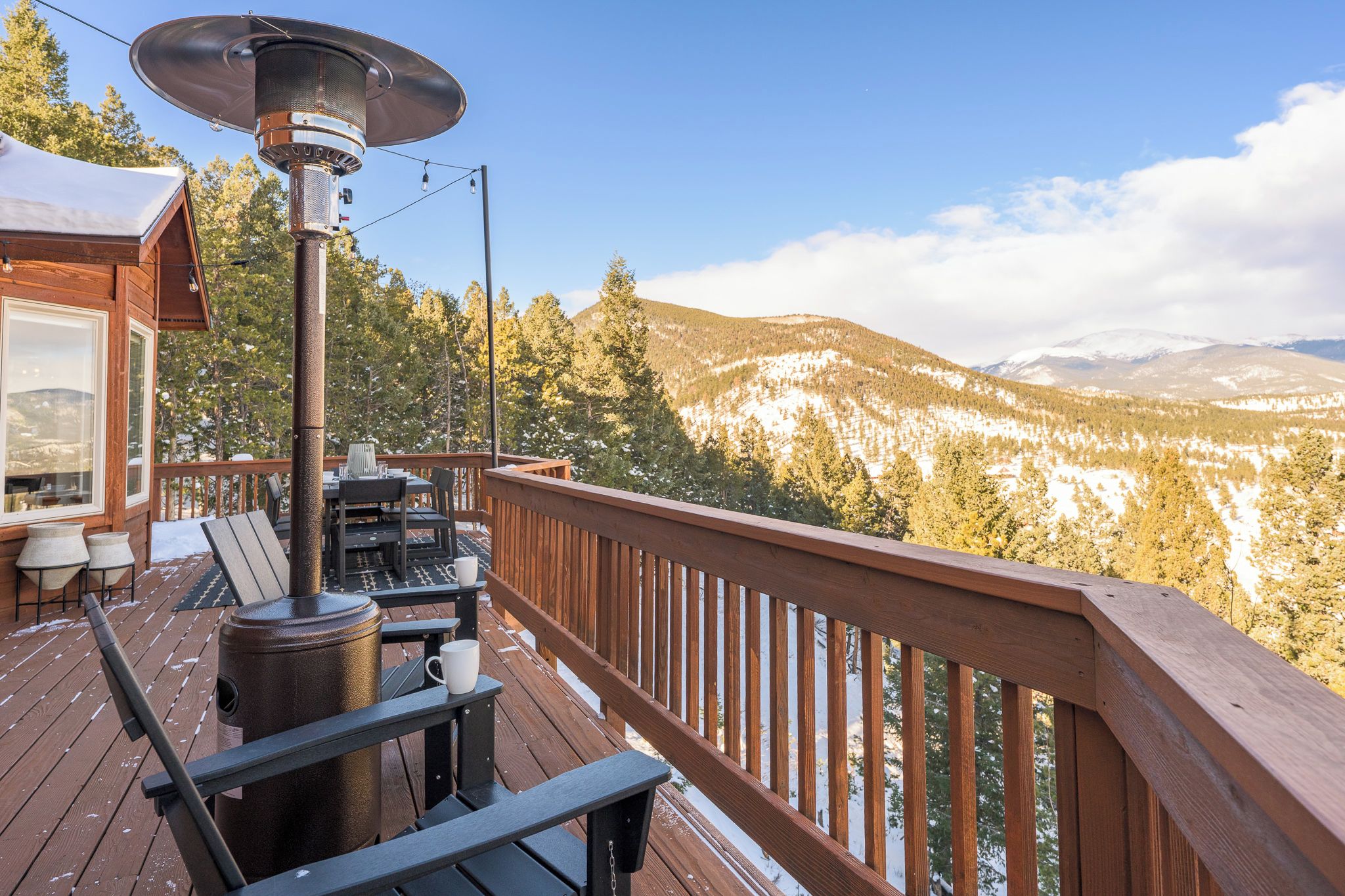 Una terraza de madera con un calentador metálico, mobiliario exterior y vistas a montañas nevadas.