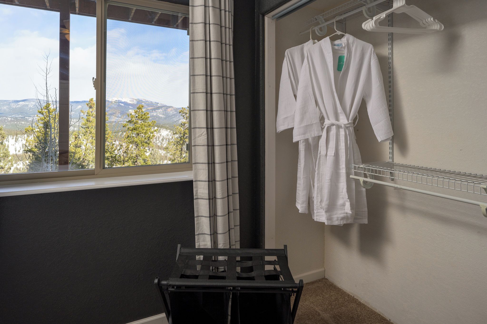 A room with a window, a black drying rack, and a white robe hanging on a wall-mounted rack.