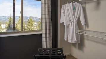 A room with a window, a black drying rack, and a white robe hanging on a wall-mounted rack.