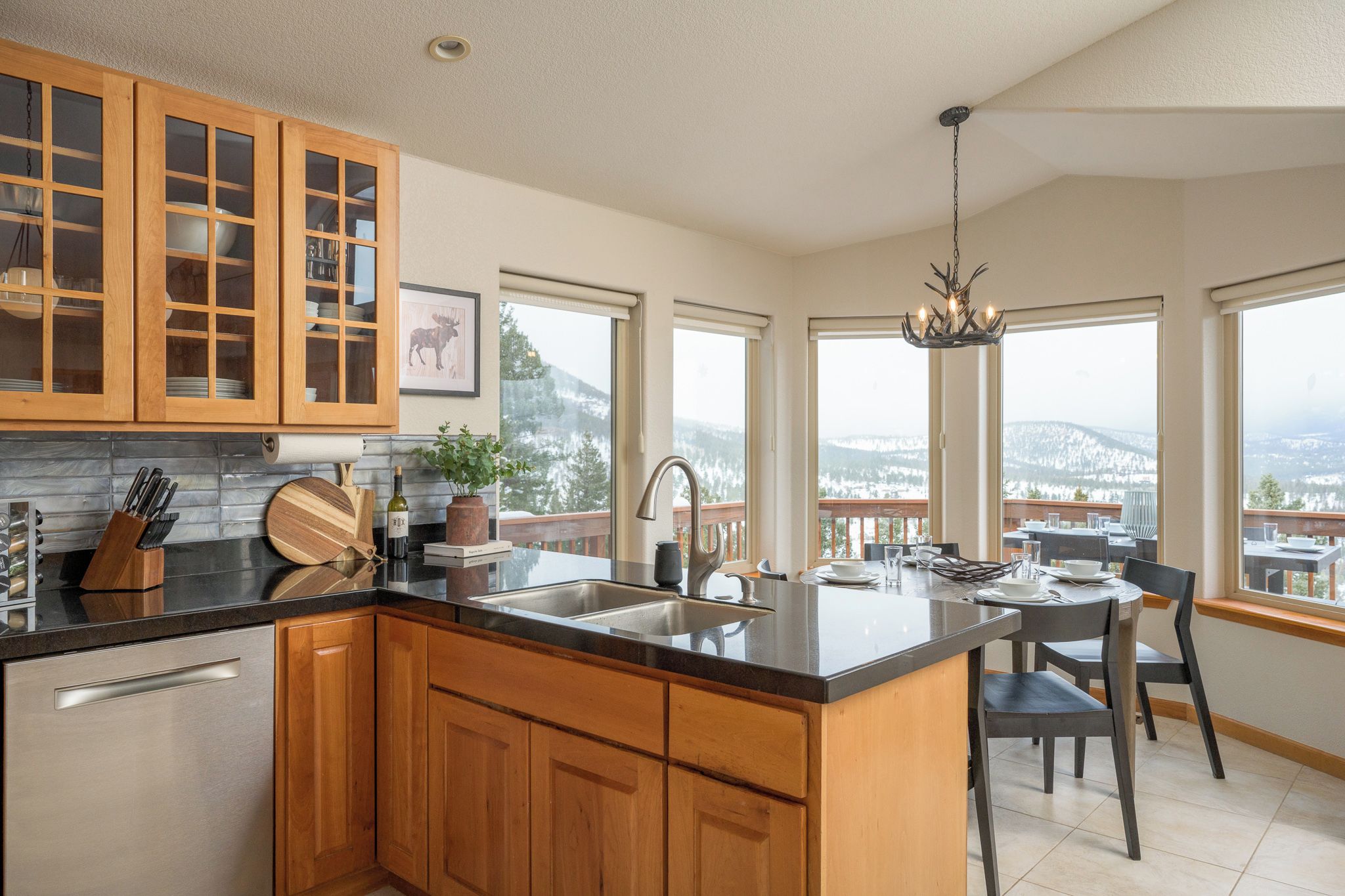 A modern kitchen with wooden cabinets, a black countertop, and a view of a snowy landscape through large windows.