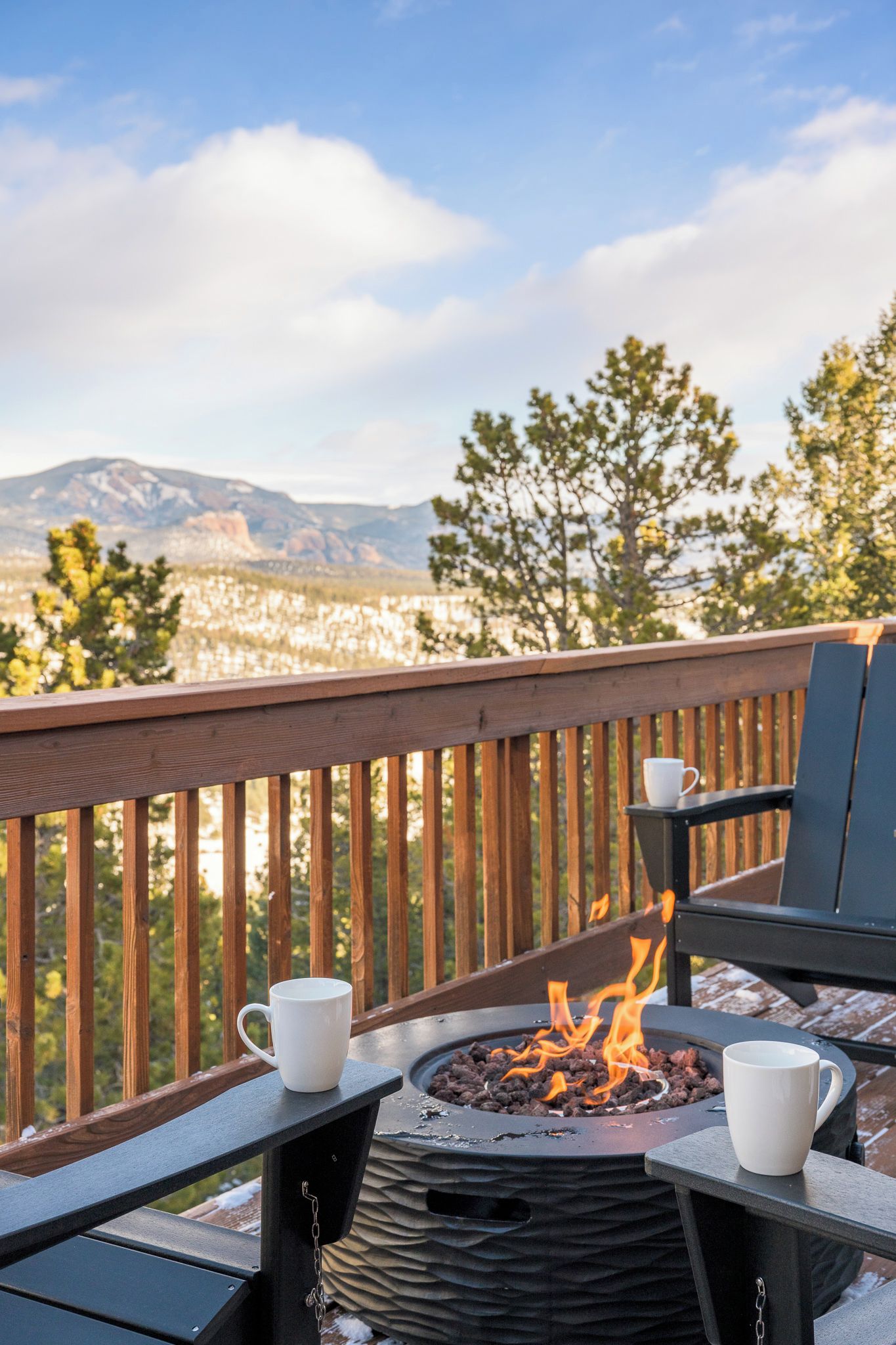 A deck with a fire pit, two chairs, and a table with two white cups.