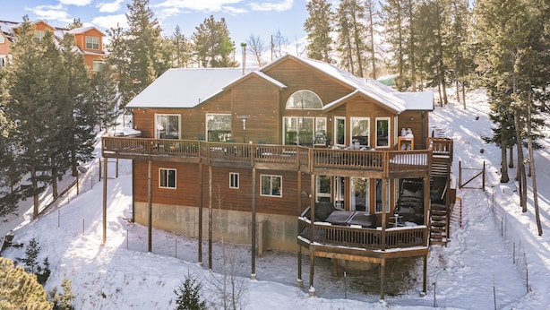 A multi-story wooden cabin with a balcony, situated on a snow-covered slope surrounded by trees. - Hilltop Haven with a Hot Tub, Game room, Poker lounge, Gym, Sauna, VIEWS (Bailey)