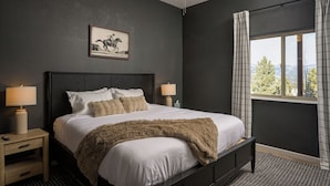 A bedroom with a bed, two bedside tables, a nightstand, a ceiling fan, a window with curtains, and a framed picture on the wall. - Hilltop Haven with a Hot Tub, Game room, Poker lounge, Gym, Sauna, VIEWS (Bailey)