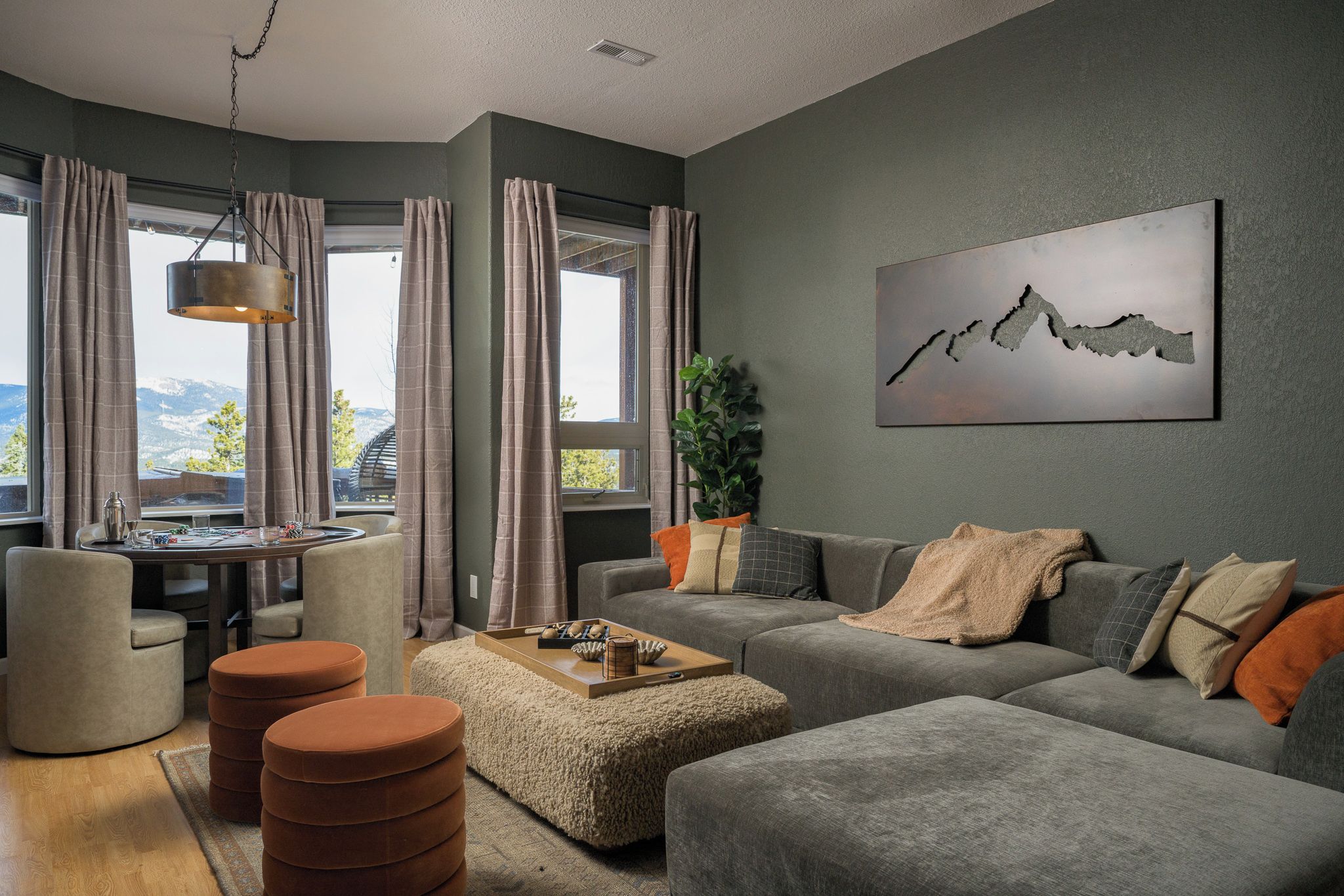 Una sala de estar moderna con un conjunto de sofá gris, una mesa de centro y vistas a montañas a través de amplios ventanales.