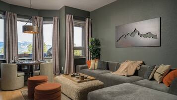 Una sala de estar moderna con un conjunto de sofá gris, una mesa de centro y vistas a montañas a través de amplios ventanales.