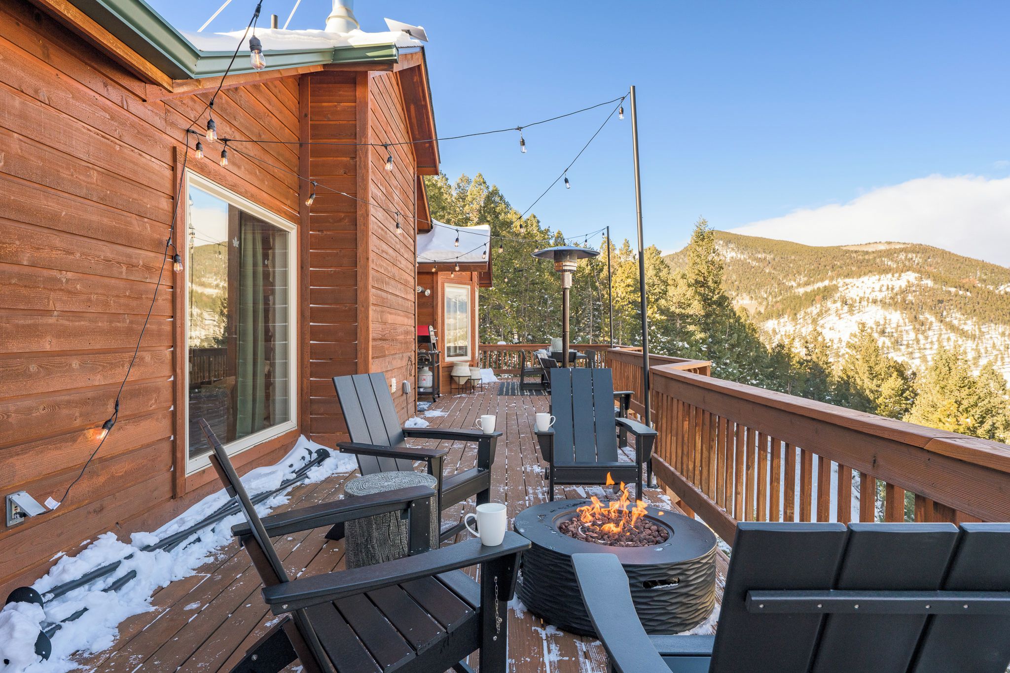 A wooden deck with outdoor seating and a fire pit, overlooking a mountainous landscape.