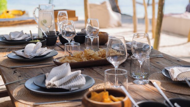 Mesa de madeira posta com pratos, tigelas e copos, indicando uma disposição para refeições.