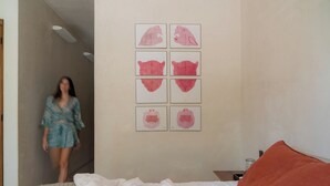 Quarto com cama, mesa de cabeceira e parede com seis obras de arte emolduradas.