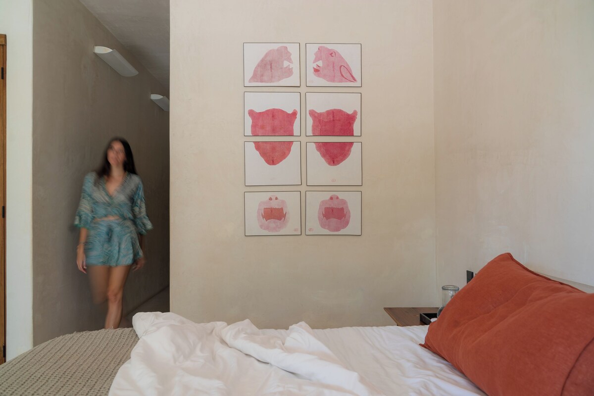 Un dormitorio con cama, mesita de noche y una pared decorada con seis obras de arte enmarcadas.