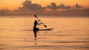 A silhouette of a person kayaking on a calm body of water during sunset.