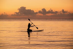 A silhouette of a person kayaking on a calm body of water during sunset.