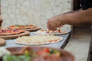 Una persona preparando pizzas sobre una encimera de mármol con diferentes ingredientes y queso.