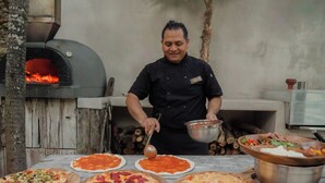 Um chef prepara pizzas numa cozinha ao ar livre com forno a lenha.