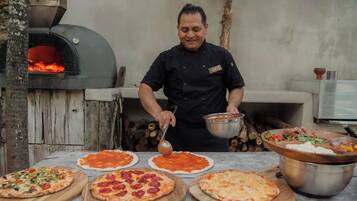 Un chef prepara pizzas en una cocina al aire libre con horno de leña.