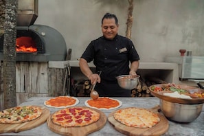 Un chef prepara pizzas en una cocina al aire libre con horno de leña.