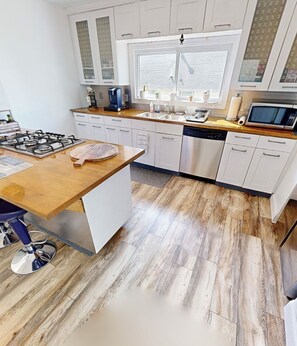 A modern kitchen with white cabinets, a wooden countertop, a gas stove, and a dishwasher.