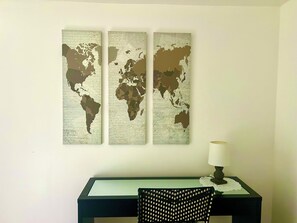 Eine Weltkarte als Wandbild über einem Schreibtisch mit einem Stuhl und einer Lampe.